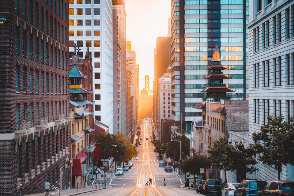 View down California Street in San Francisco, California with Chinatown pagoda buildings and golden hour sky in background.